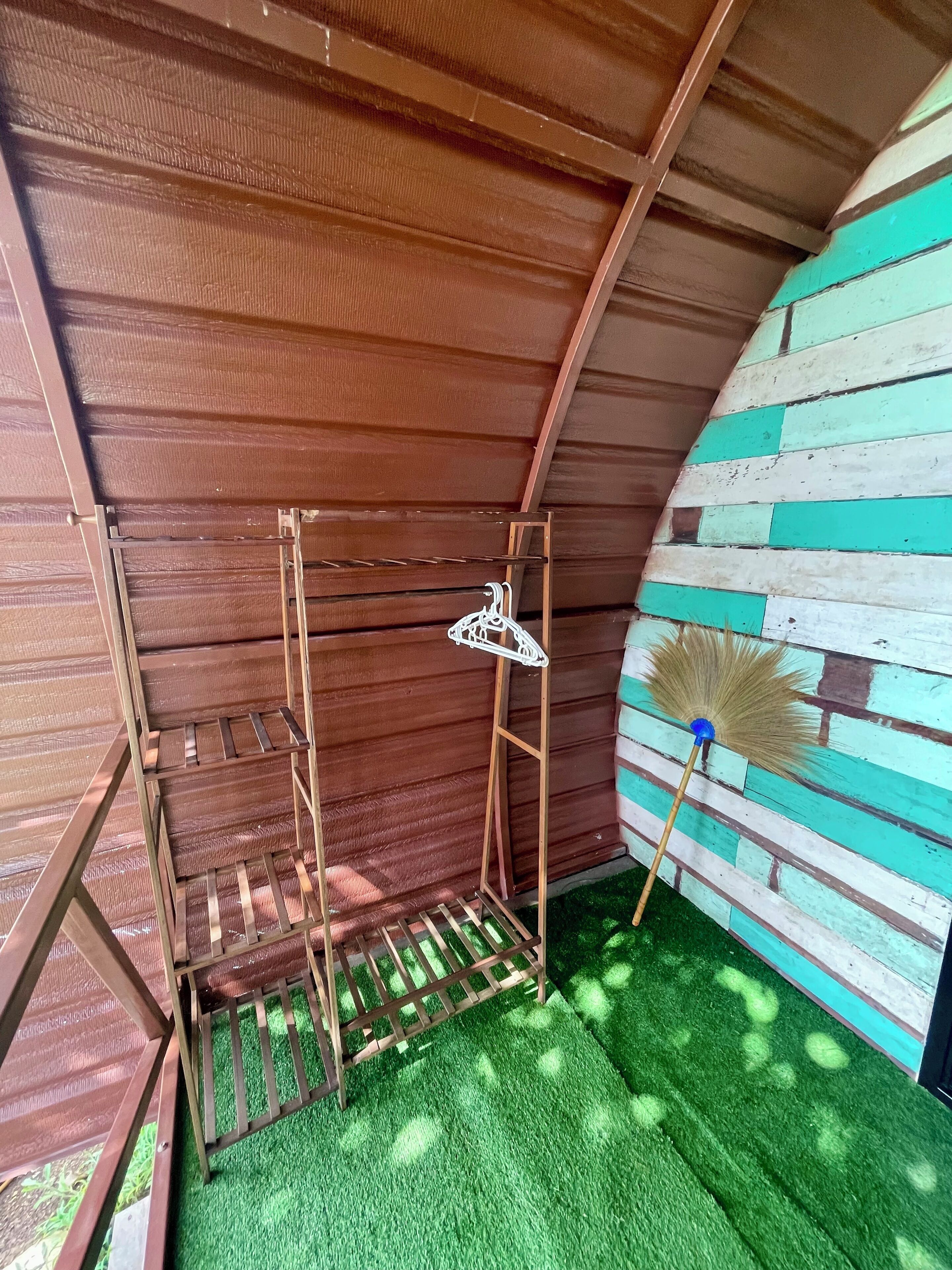 A wooden shed with a metal rack and a broom.