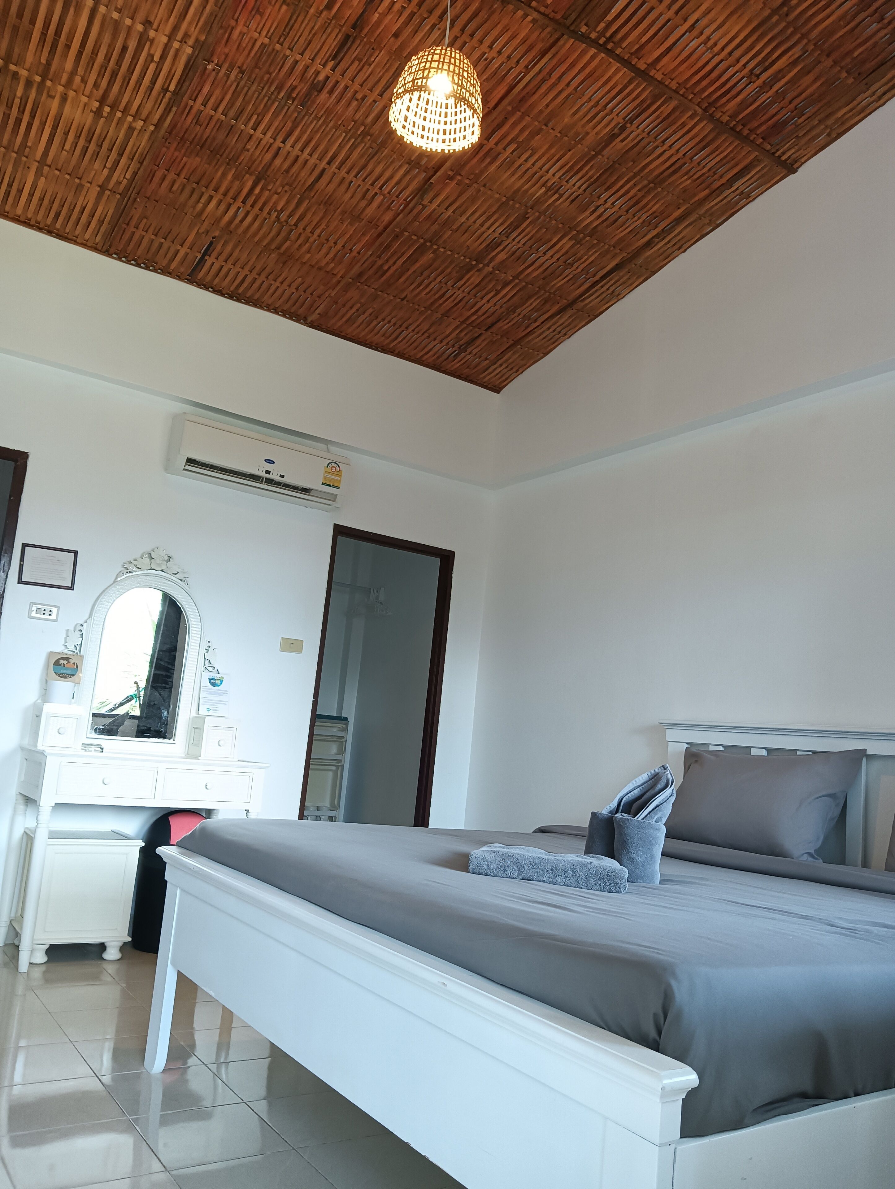 A bedroom with a bed, bedside table, mirror, dresser, and an air conditioning unit.