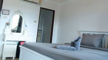 A bedroom with a bed, bedside table, mirror, dresser, and an air conditioning unit.