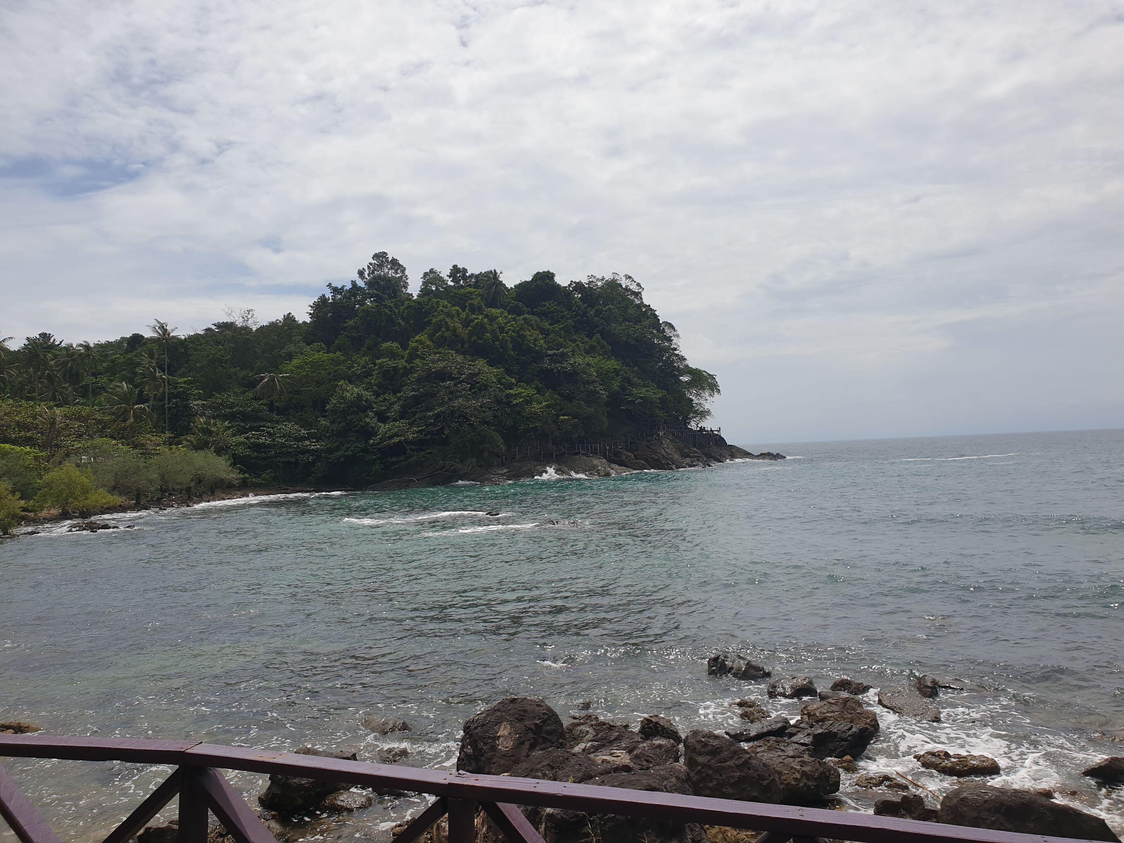 A coastal view with a rocky shoreline, clear water, and a forested island.