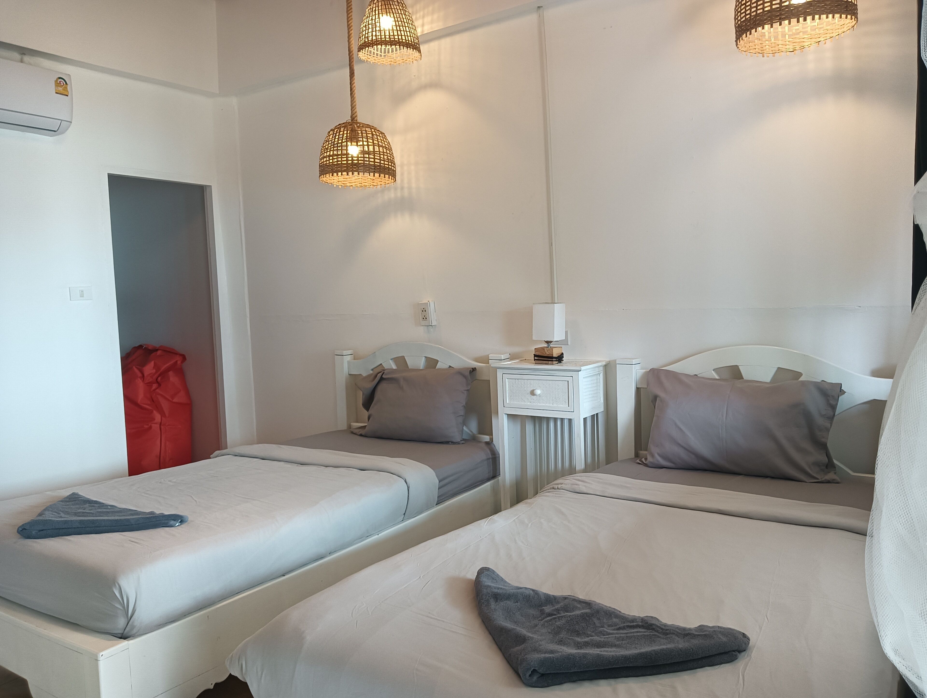 A hotel room with two beds, a nightstand with a lamp, and a red bag in the corner.