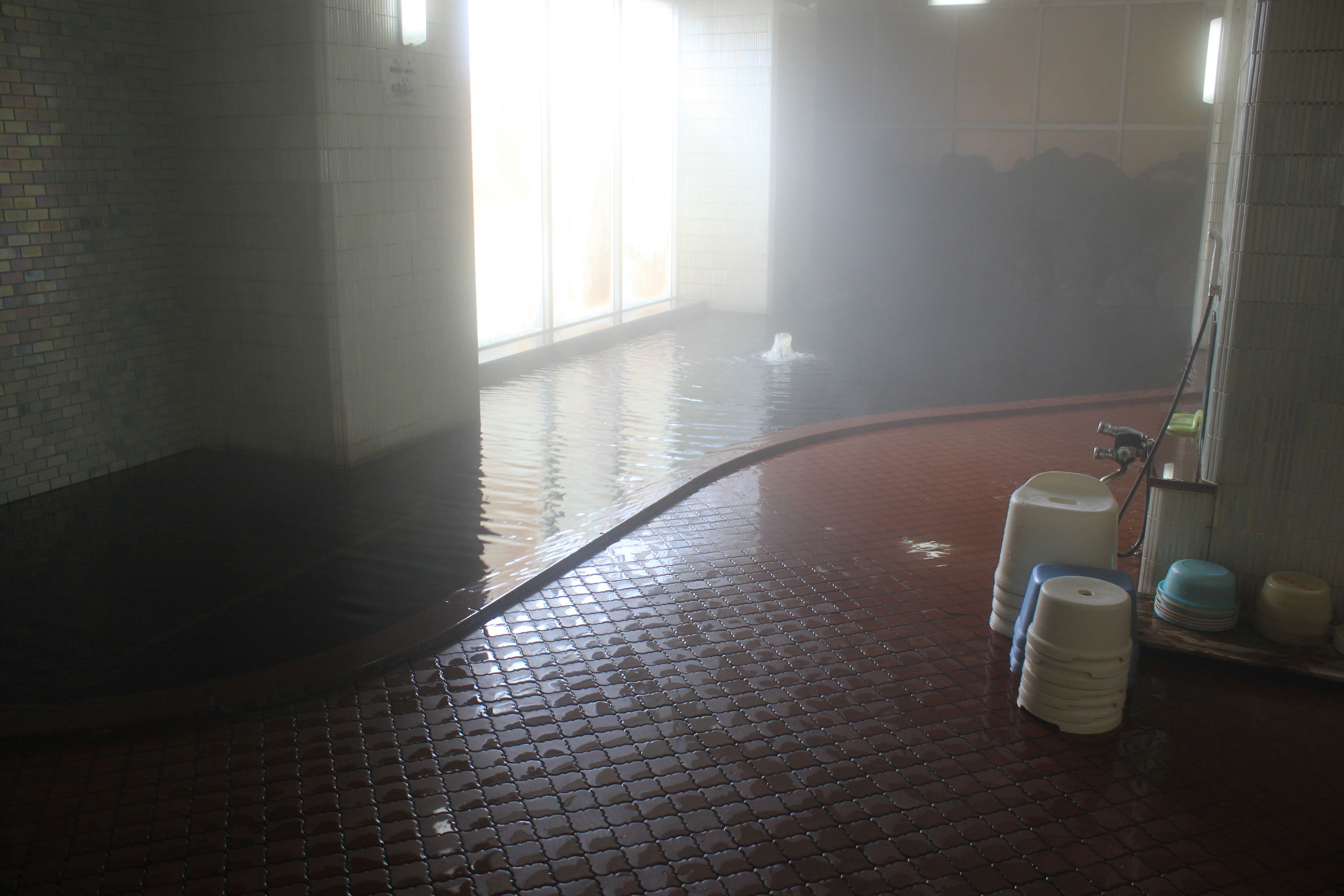 A wet tiled floor with a steam shower, a water dispenser, and a tiled wall with a window.
