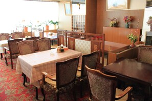 A restaurant with wooden tables and chairs, a red carpeted floor, and potted plants on the walls. - Hot Spring Hotel Boston (Obihiro)