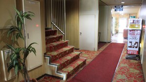A hotel corridor with a red carpet, a staircase, a potted plant, and a sign for a coffee shop. - Hot Spring Hotel Boston (Obihiro)