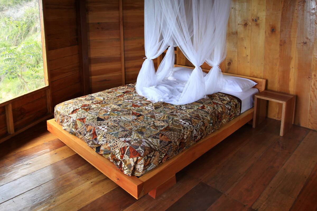 Een houten bed met een gebedrukte sprei, een baldakijn en een klein nachtkastje.