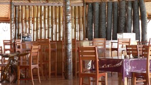 A restaurant with bamboo columns, wooden chairs, and tables. - Waecicu Eden Beach Hotel (Labuan Bajo)