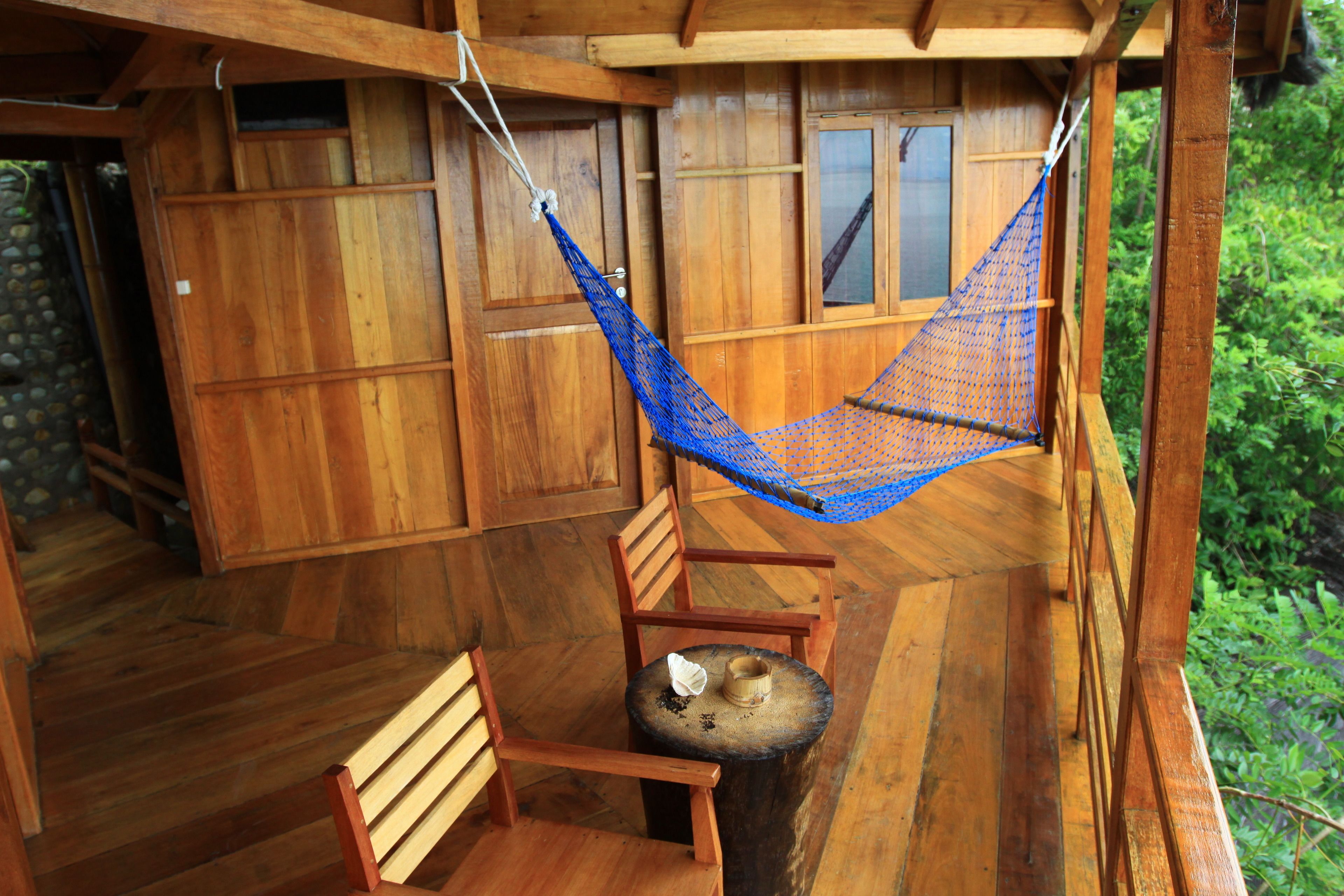 A wooden deck with a hammock, a wooden chair, and a small round table.