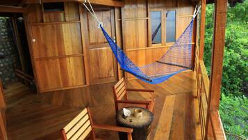 A wooden deck with a hammock, a wooden chair, and a small round table.
