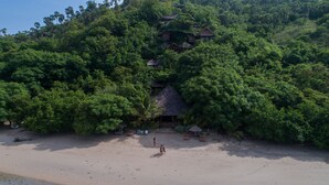 A beach with a thatched-roof hut and several wooden cabins surrounded by dense forest. - Waecicu Eden Beach Hotel (Labuan Bajo)