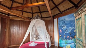 A room with a wooden floor, a bed with a canopy, a mural of marine life, and a wooden cabinet. - Waecicu Eden Beach Hotel (Labuan Bajo)