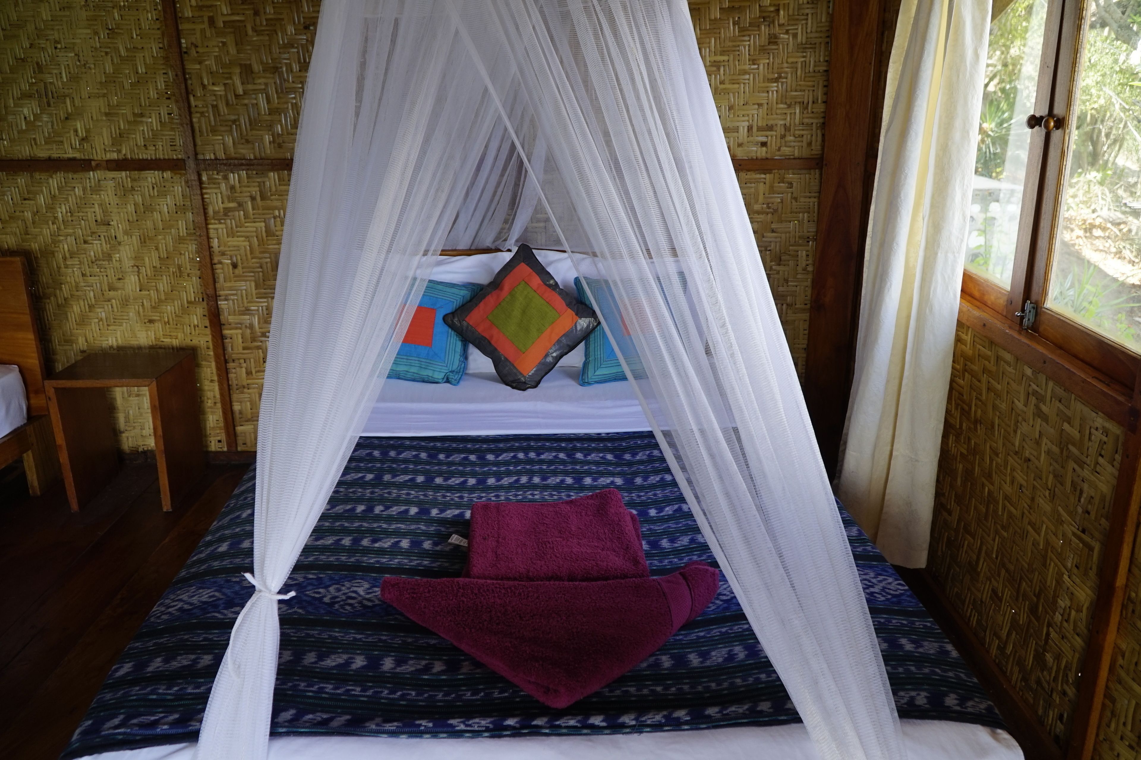 A bed with a canopy, a patterned bedspread, and a purple towel.