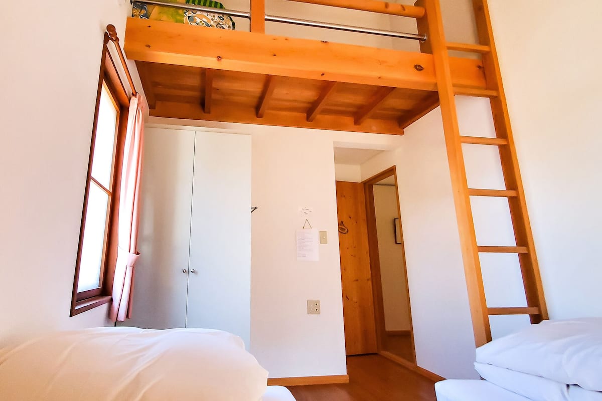 Un dormitorio con una cama litera, una escalera de madera, una puerta y una ventana con cortinas.