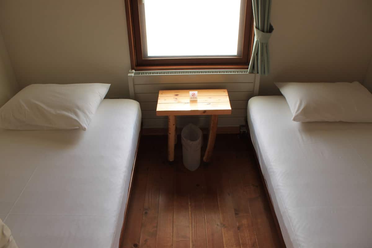 Una habitación con dos camas individuales, una mesita de madera y un ventanal con cortinas.