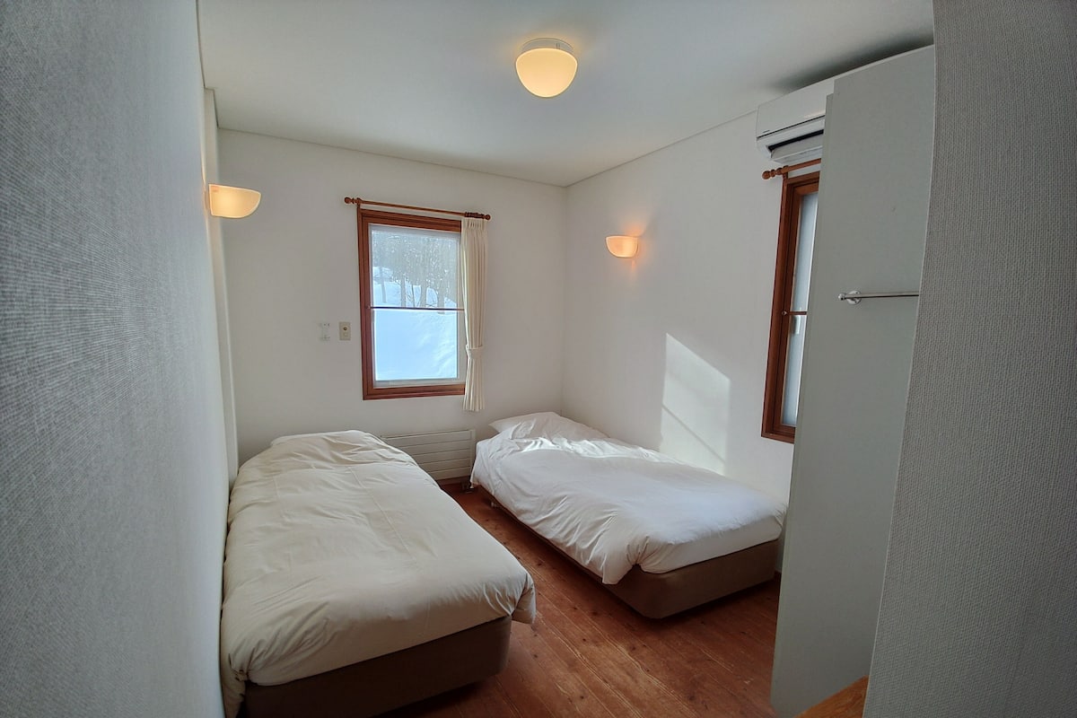 Una habitación pequeña y limpia con dos camas individuales, un radiador y una ventana con cortinas.