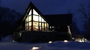 A large, modern house with a prominent glass facade and a steeply pitched roof, surrounded by snow. - Pension Gooseberry (Furano)