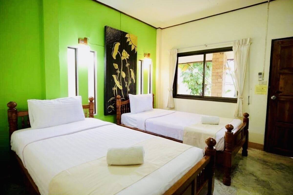A room with two single beds, a green wall, a window with curtains, and a wooden door.