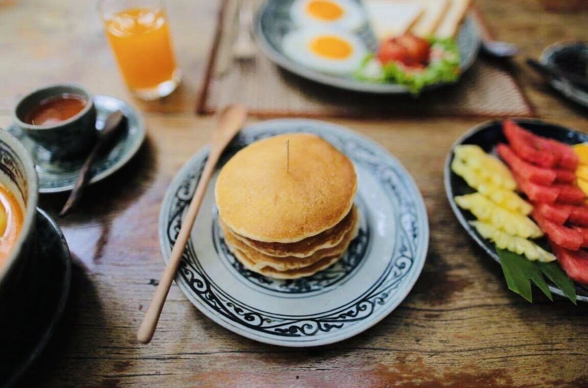 A breakfast setting with pancakes, eggs, and fruit on a wooden table.