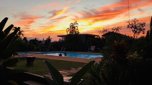 A swimming pool with lounge chairs and a gazebo, surrounded by tropical plants and a sunset sky. - Sabaidee House (Sukhothai)