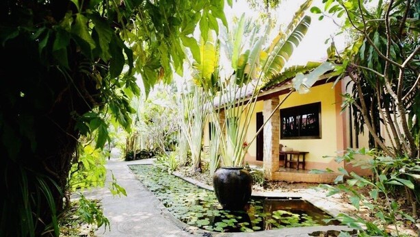 A pathway leading to a building surrounded by lush greenery and a small pond with lily pads. - Sabaidee House (Sukhothai)