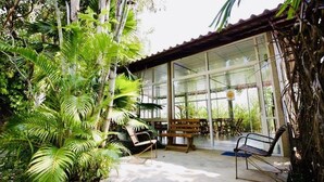 A covered outdoor seating area with benches and tables, surrounded by lush greenery. - Sabaidee House (Sukhothai)