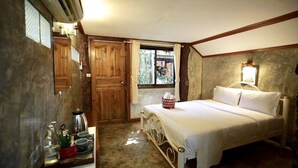 A bedroom with a bed, a bedside table with a kettle, cups, and a red container. There is a window with curtains and a view of greenery outside. - Sabaidee House (Sukhothai)