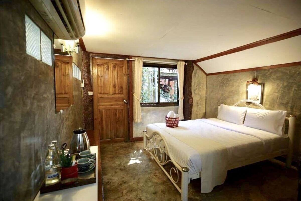 A bedroom with a bed, a bedside table with a lamp, a window with curtains, and a wooden door.