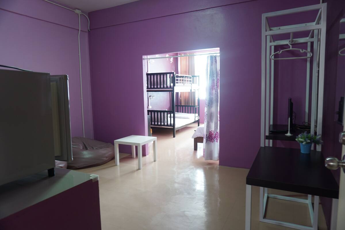 A room with a bunk bed, a small table, a chair, and a desk with a plant.