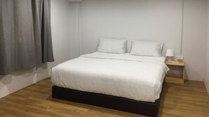 Un dormitorio con una cama, dos almohadas, una mesita de noche con lámpara y un enchufe.
