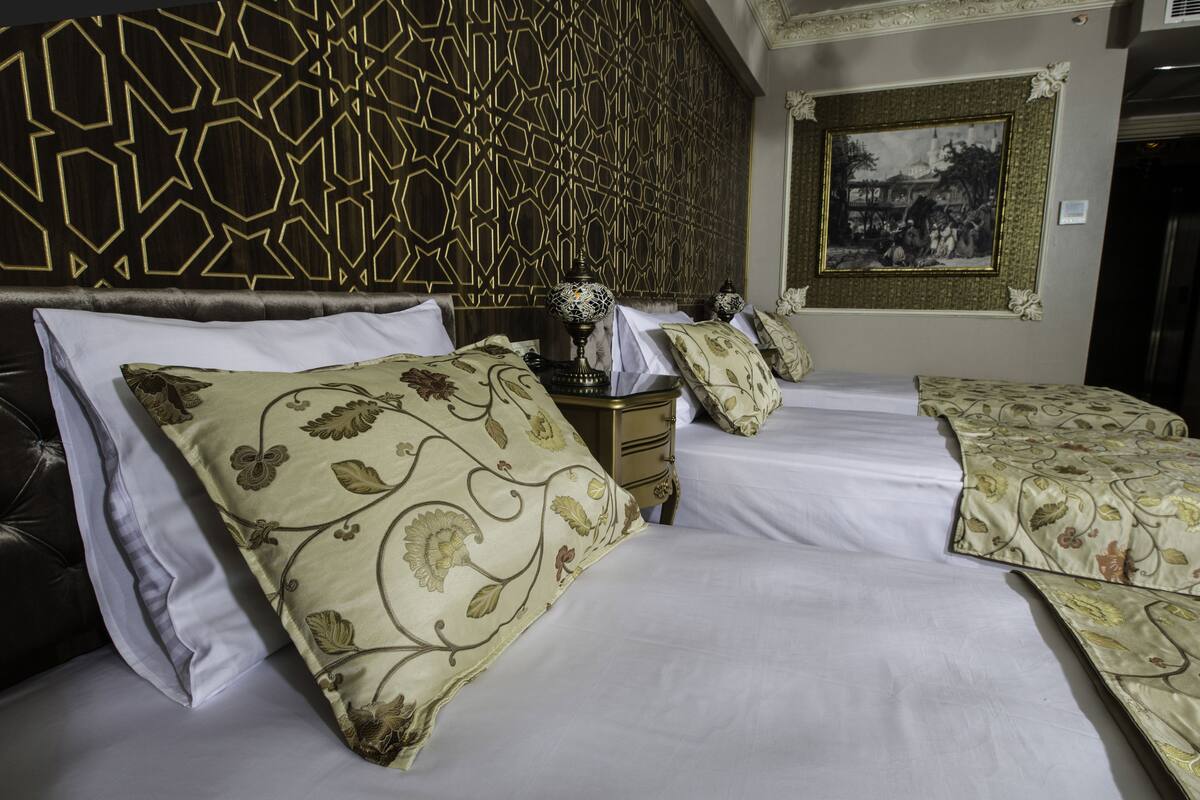 A hotel room with a large bed, multiple pillows, a nightstand, and a decorative wall panel.