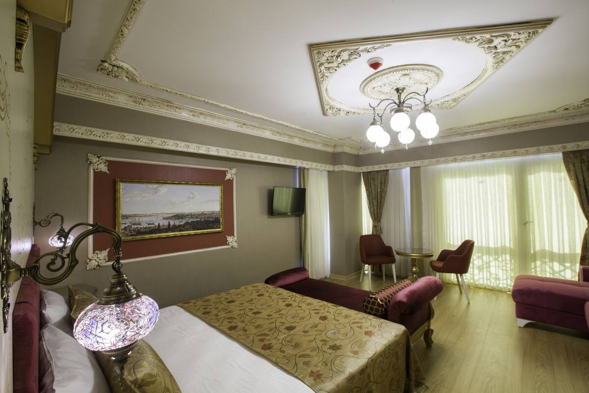 A hotel room with a bed, a chandelier, a television, and two chairs.