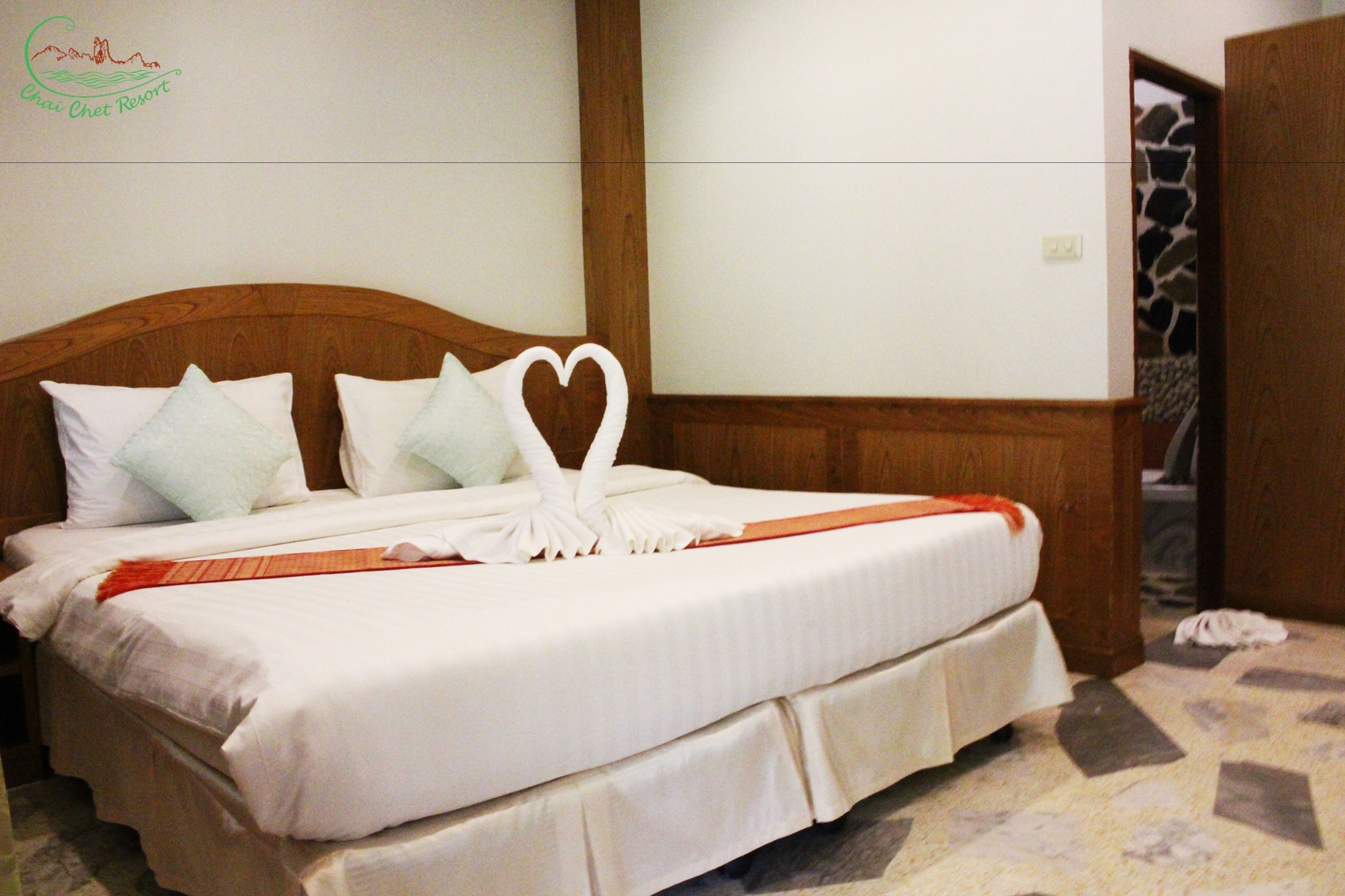 A neatly made bed with a heart-shaped towel decoration, white bedding, and a wooden headboard.
