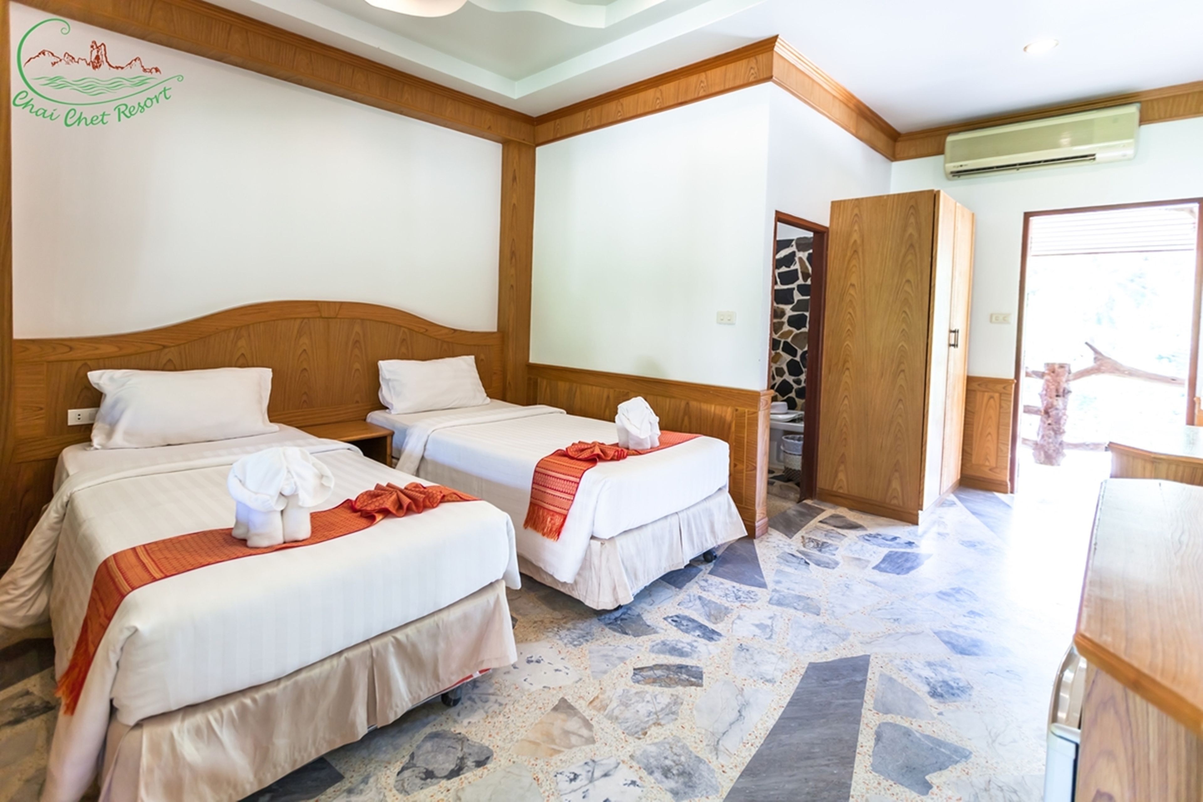Een hotelkamer met twee bedden, een vloer van stenen tegels, houten hoofdeinden en een wandairconditioning.