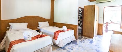 Een hotelkamer met twee bedden, een vloer van stenen tegels, houten hoofdeinden en een wandairconditioning.