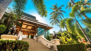 A modern building with a glass facade, surrounded by lush greenery and palm trees. - Chai Chet Resort Koh Chang (Ko Chang)