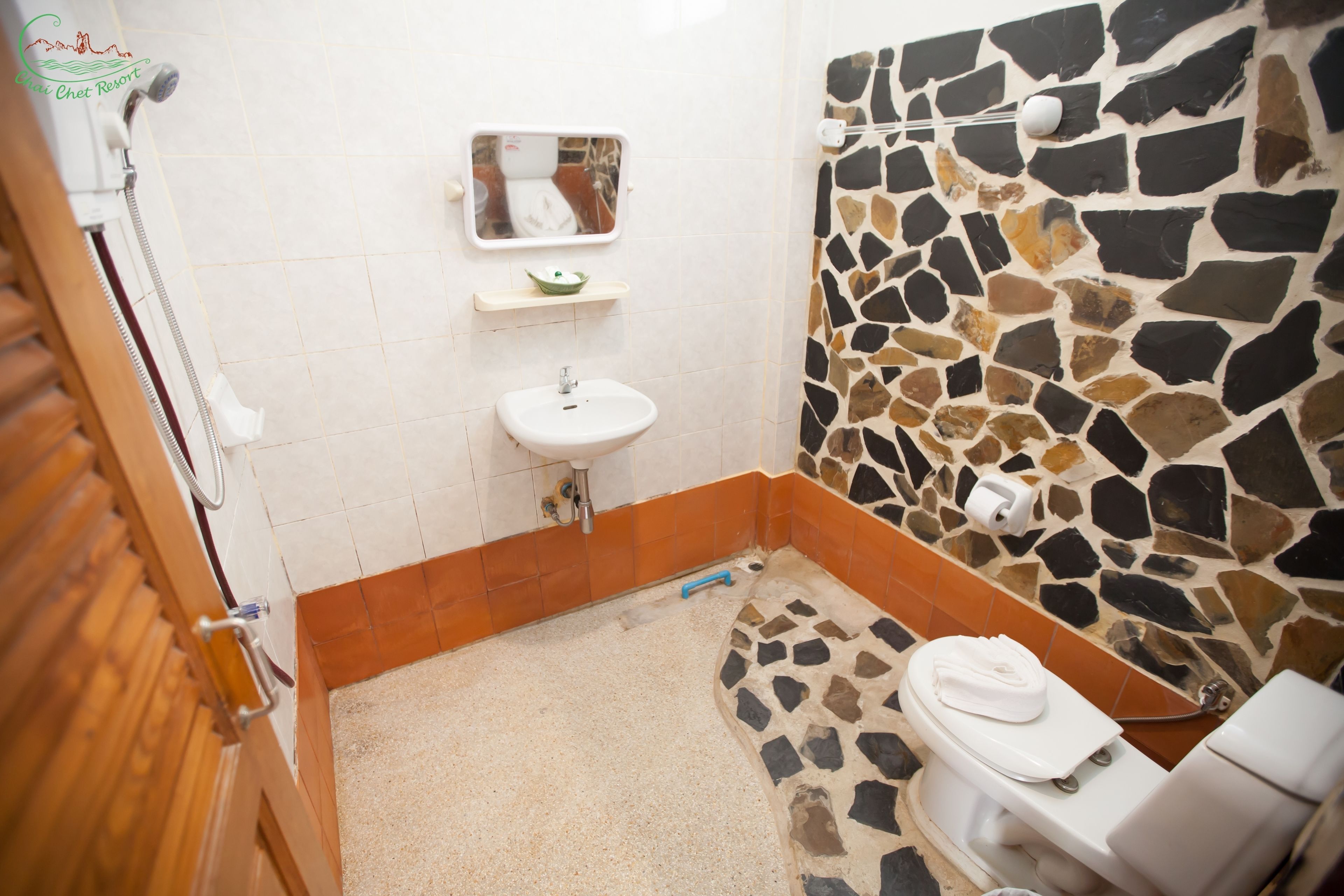 Une salle de bain avec un mur en pierre, un lavabo blanc et des toilettes.