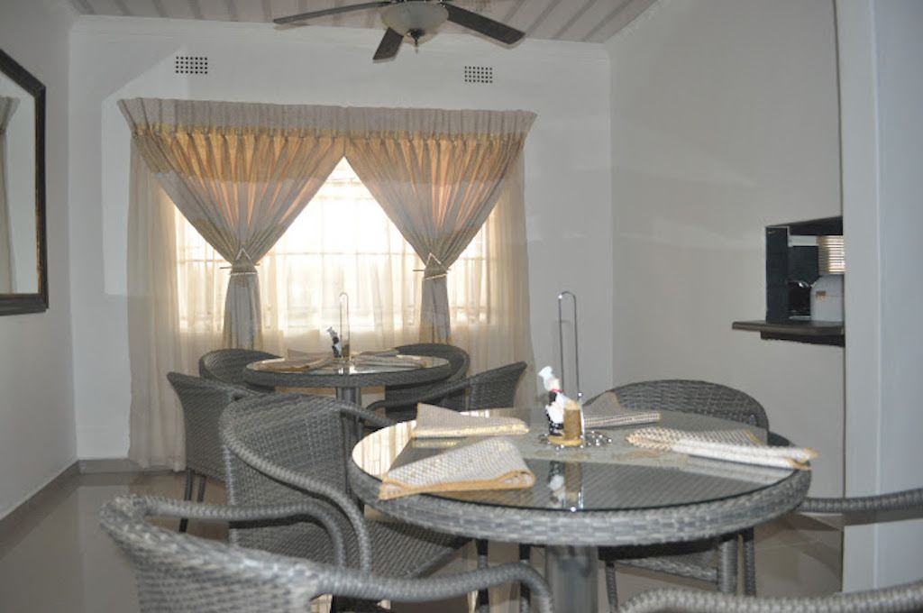 A dining area with round tables and wicker chairs, a ceiling fan, and a window with sheer curtains.