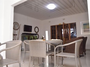 A dining area with wicker chairs and a table, a television on the wall, and a window with a view. - Crown Guest Lodge (Francistown)