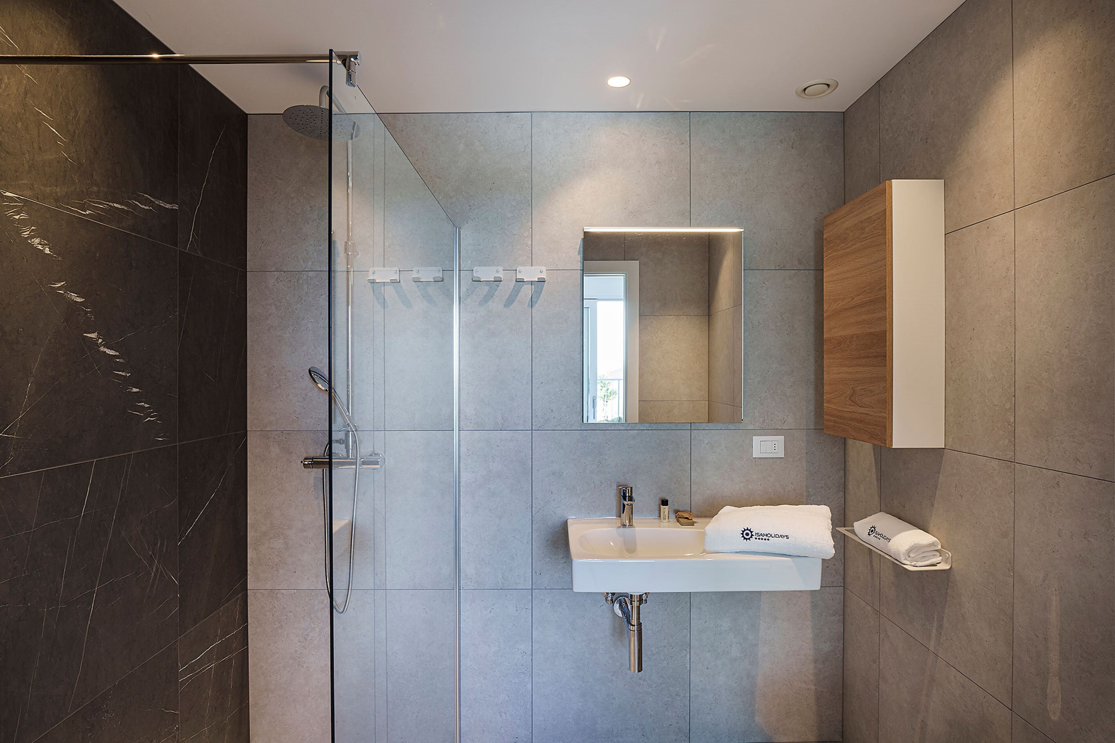 Un bagno moderno con cabina doccia in vetro, lavabo bianco e mobile vanitario in legno.