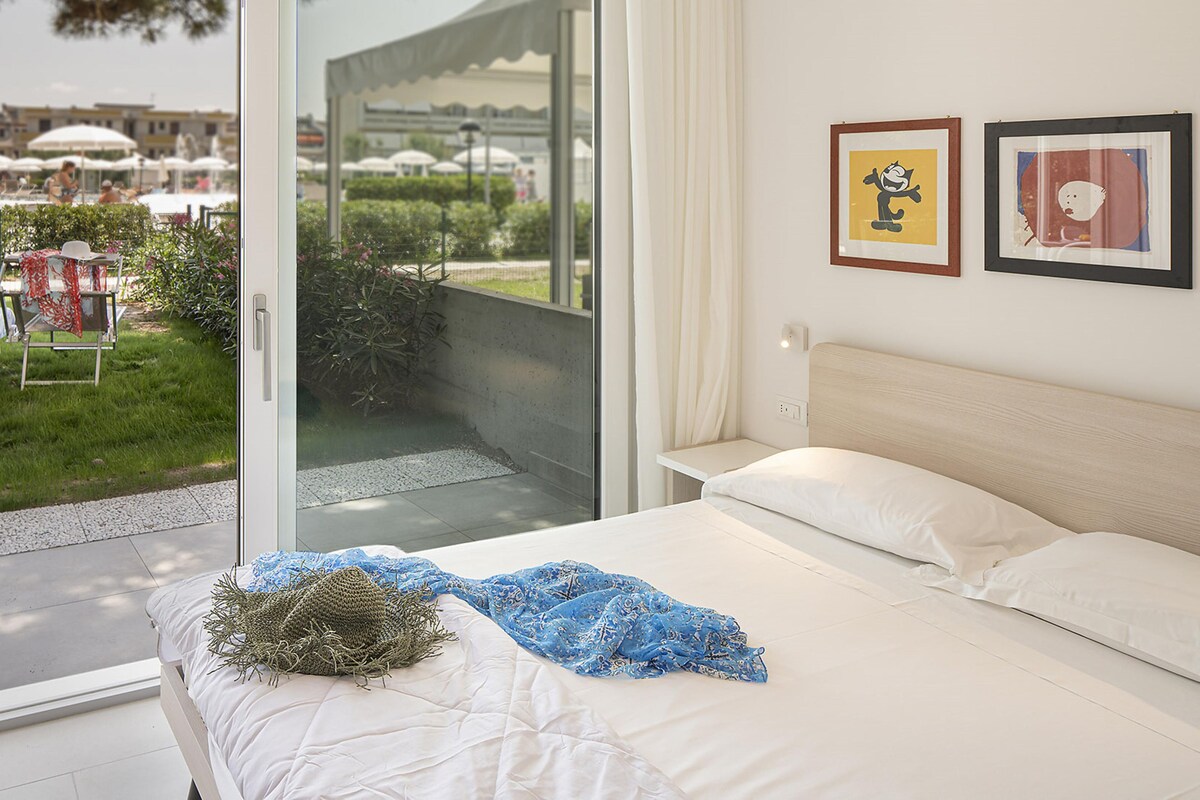 A bedroom with a bed, a view of an outdoor area with umbrellas, and two framed pictures on the wall.