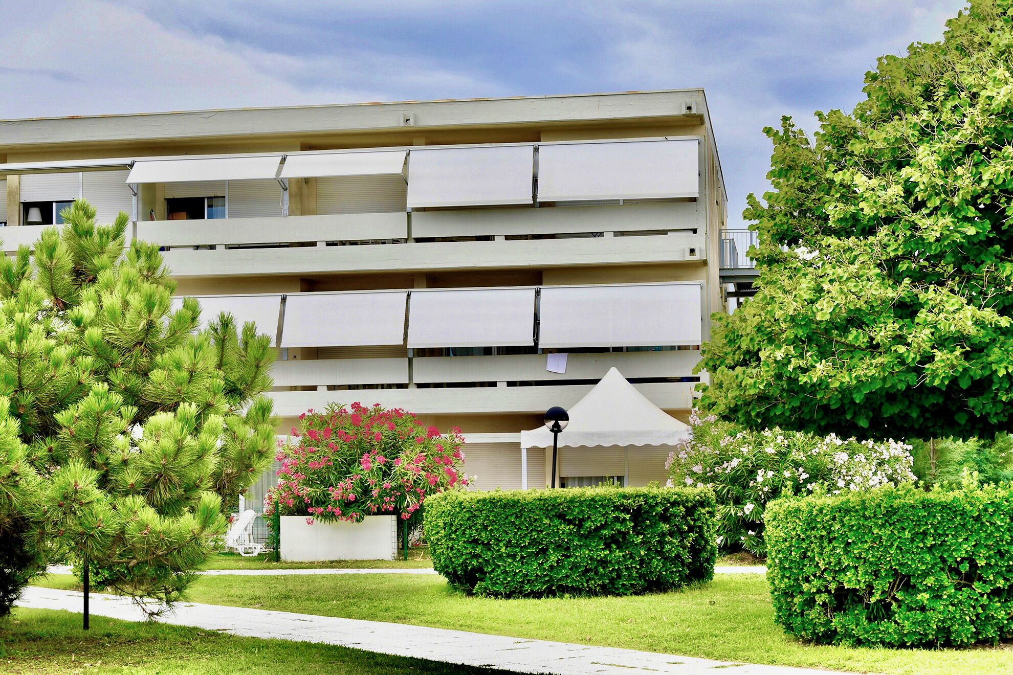 Un edificio de varios pisos con balcones, rodeado de vegetación cuidada y un cielo despejado.