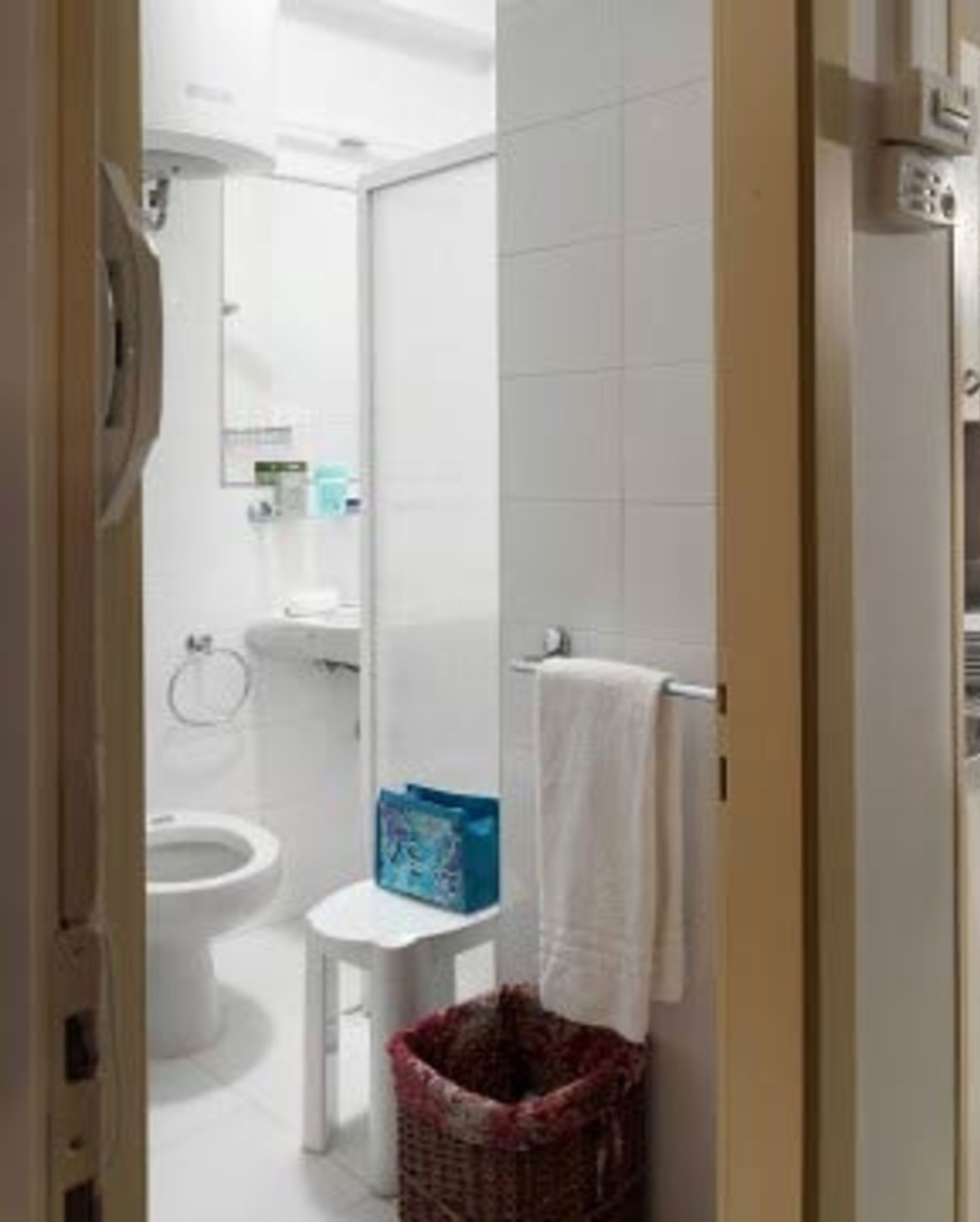 Un baño con inodoro, un taburete pequeño, una cesta y un perchero para toallas.