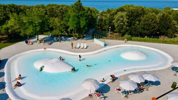 Una piscina con due grandi scivoli acquatici bianchi, circondata da lettini e ombrelloni.