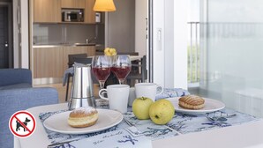 Una tavola imbandita per la colazione con pasticcini, frutta e bevande, con una cucina sullo sfondo e un cartello che indica il divieto di animali domestici.