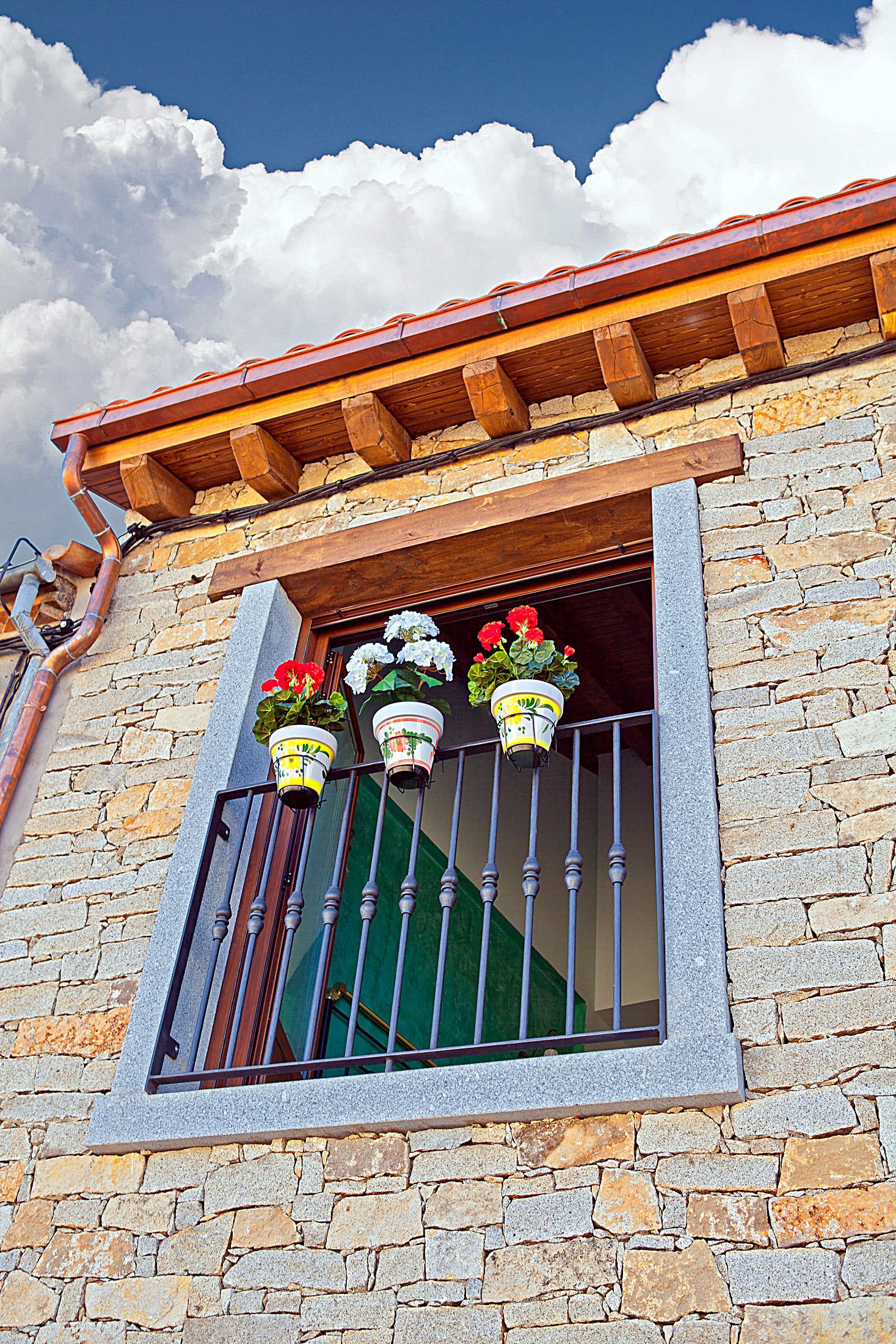 A stone building with a window featuring a metal railing and potted plants.