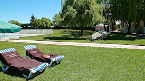 Two lounge chairs with towels, a paved walkway, and a large rock in a grassy area with trees and a building in the background. - Casa Rural Antonio (Vitigudino)
