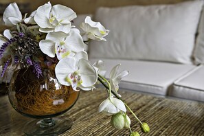 A glass vase with white orchids and purple flowers on a wooden table.