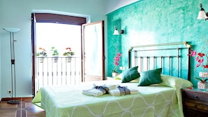 A room with a bed, a nightstand, a floor lamp, and a view of the outside balcony with potted plants. - Casa Rural Antonio (Vitigudino)