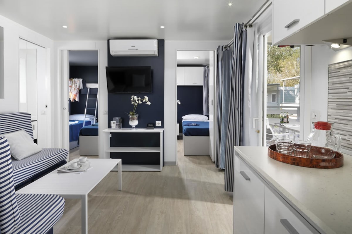 Une pièce compacte et moderne, comprenant un canapé, une petite table, un téléviseur et un coin cuisine.