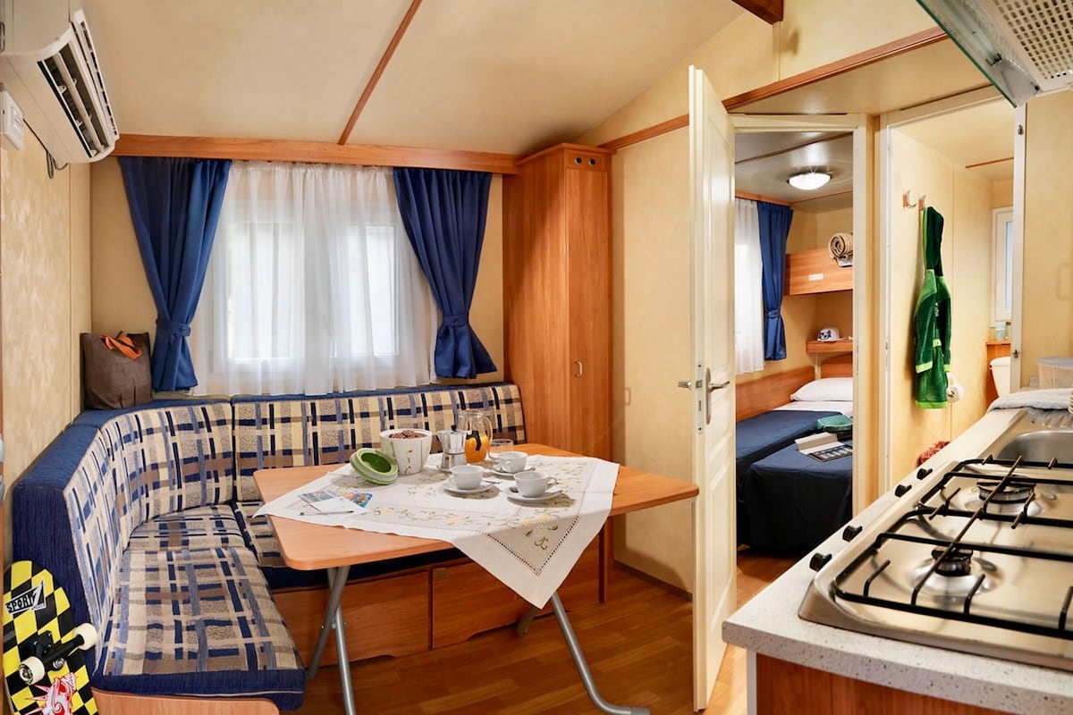 Un intérieur de camping-car compact comprenant un coin cuisine, un espace repas et un espace nuit.