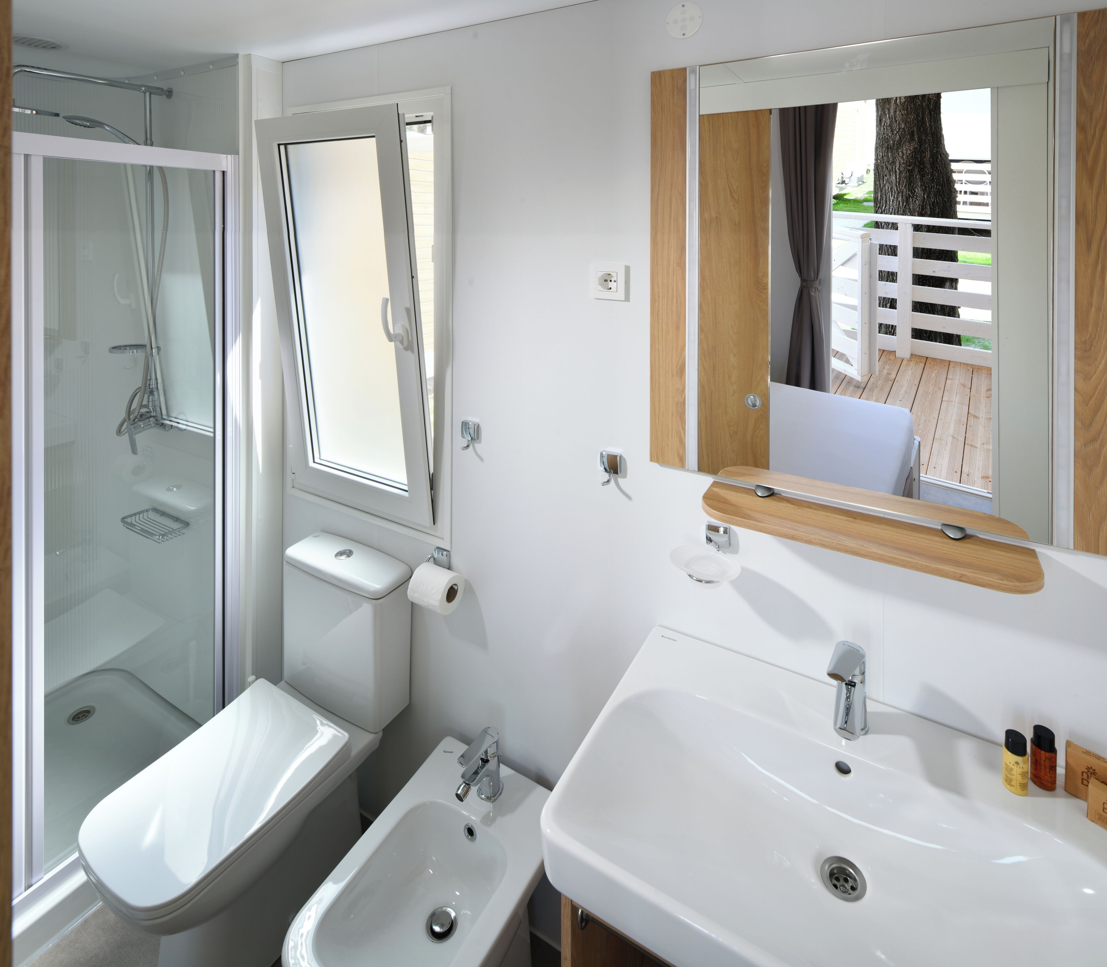 A modern bathroom with a glass-enclosed shower, a toilet, a bidet, and a sink with a mirror above.